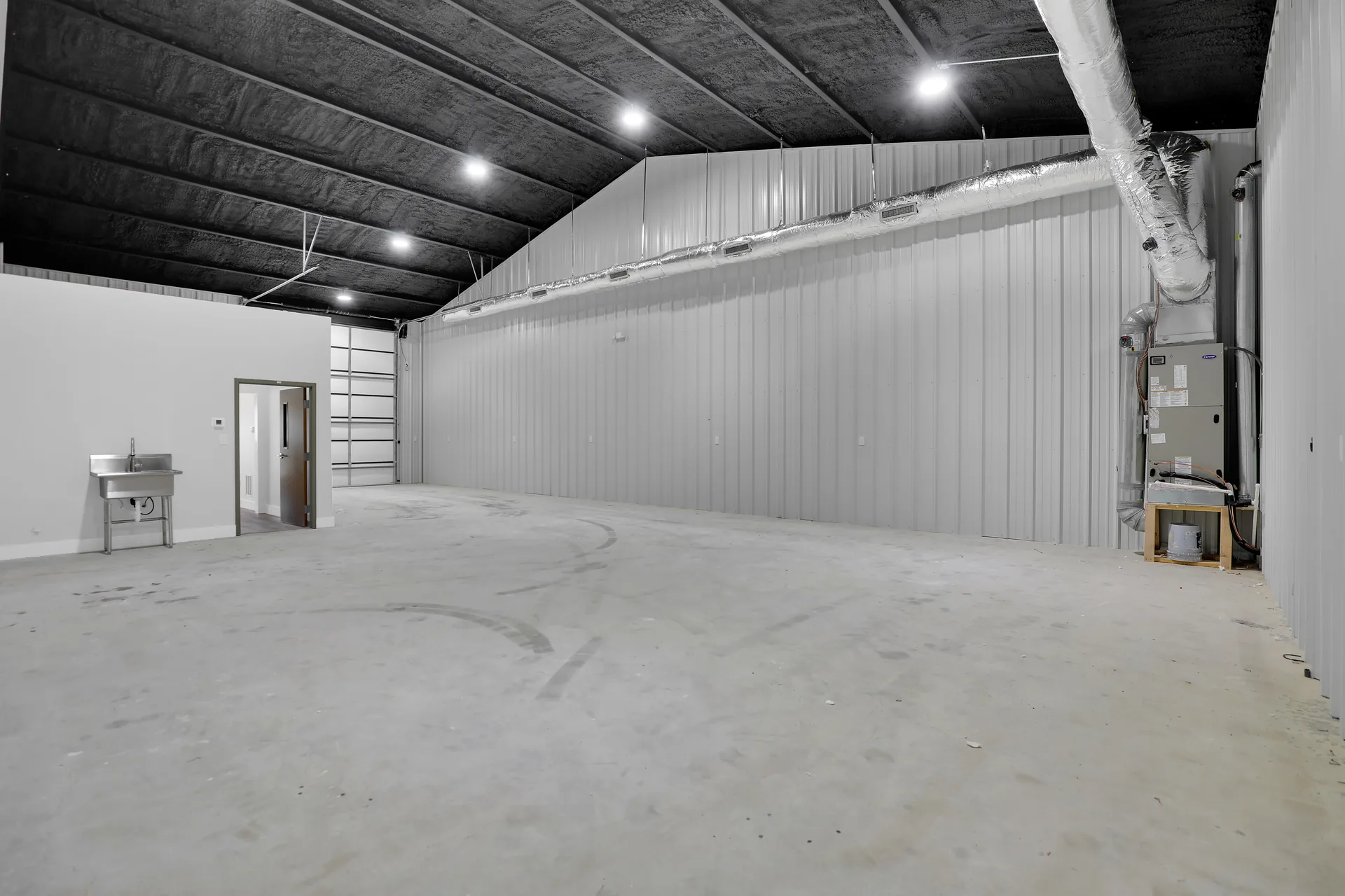 Warehouse space with overhead door, high ceiling, utility area, and access to finished interior rooms